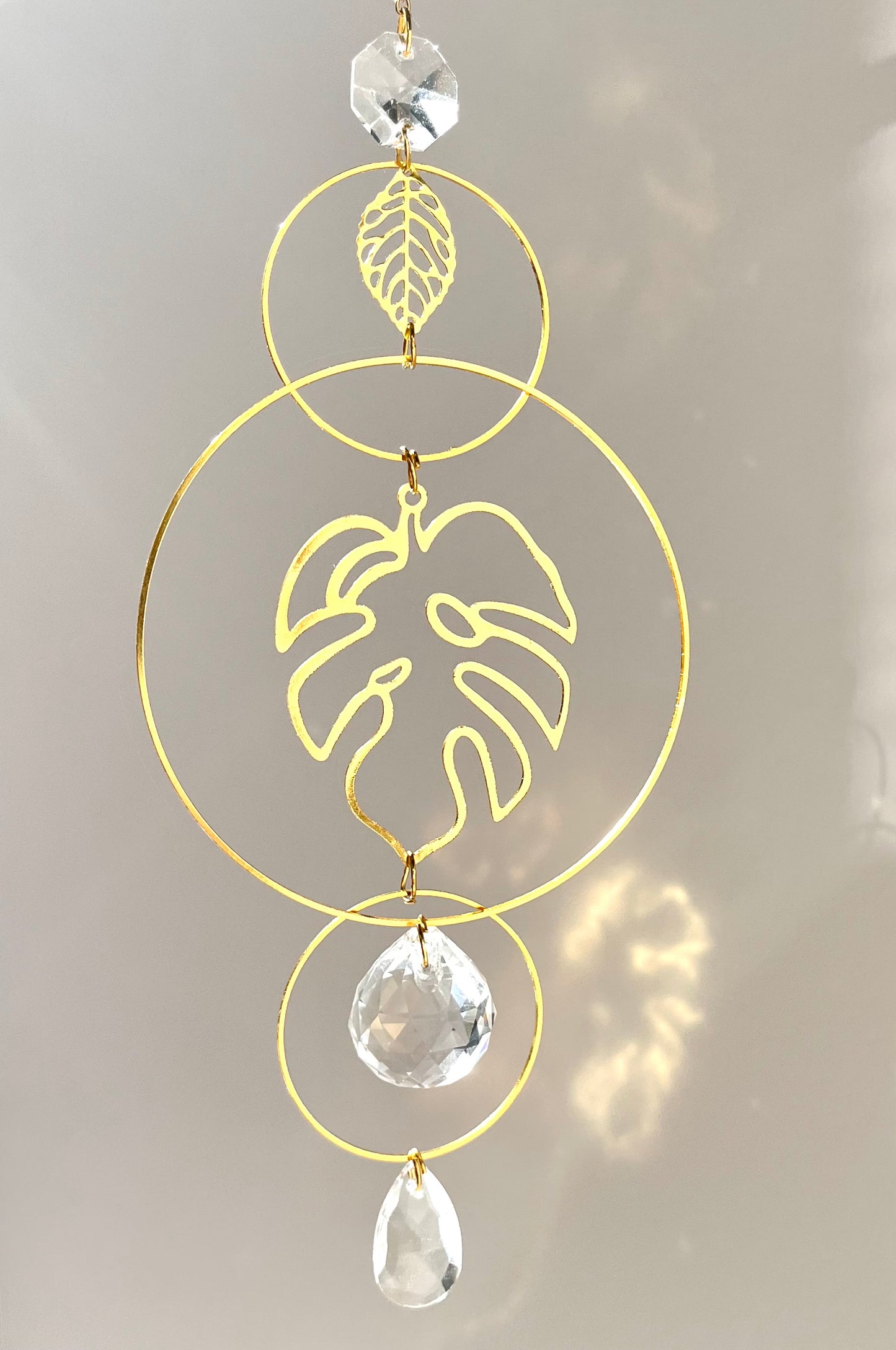 Decorative hanging ornament with gold leaf design and crystal elements on a light gray background