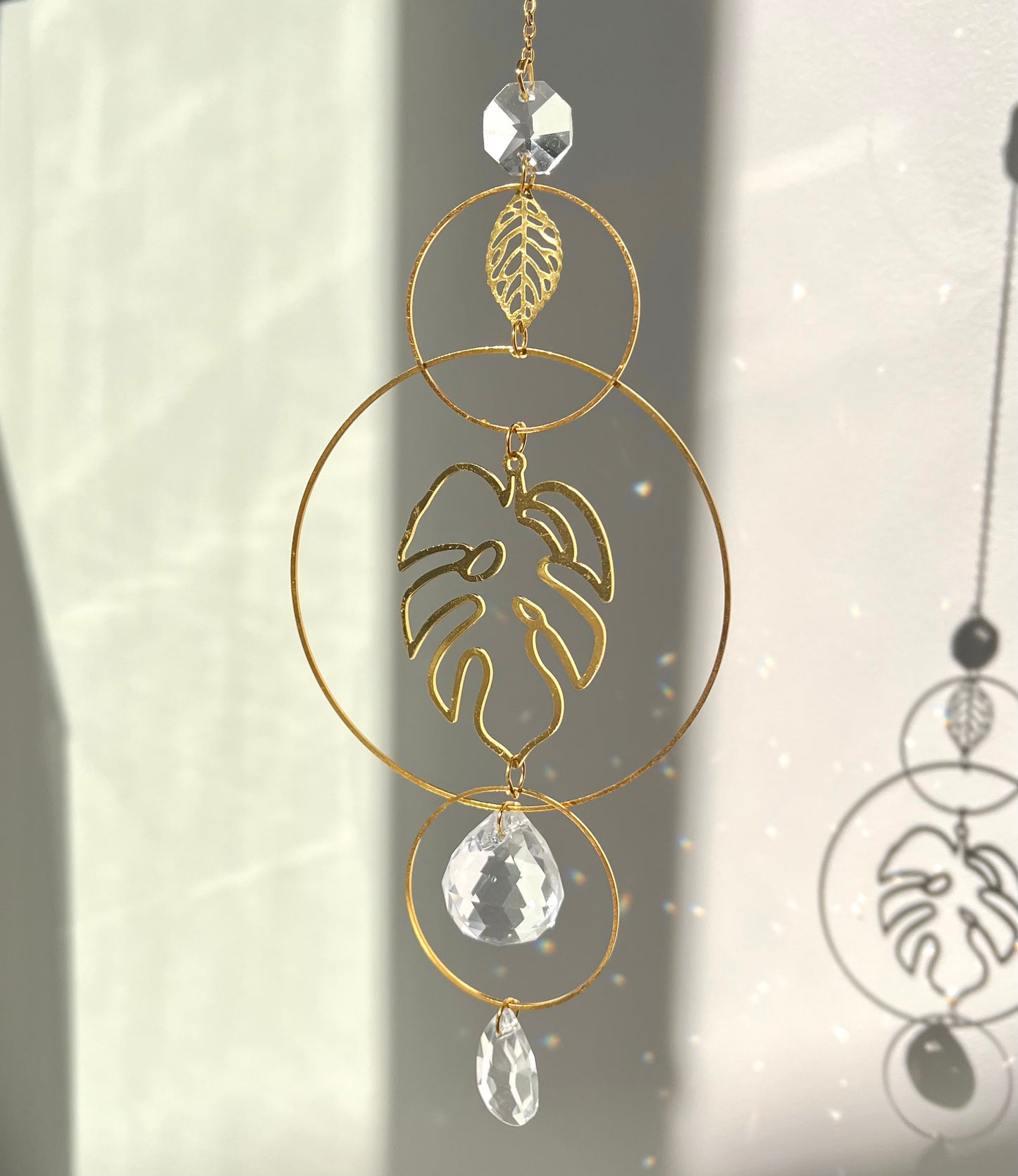 Decorative hanging ornament with gold loops, leaf design, and crystal-like elements on a light background.