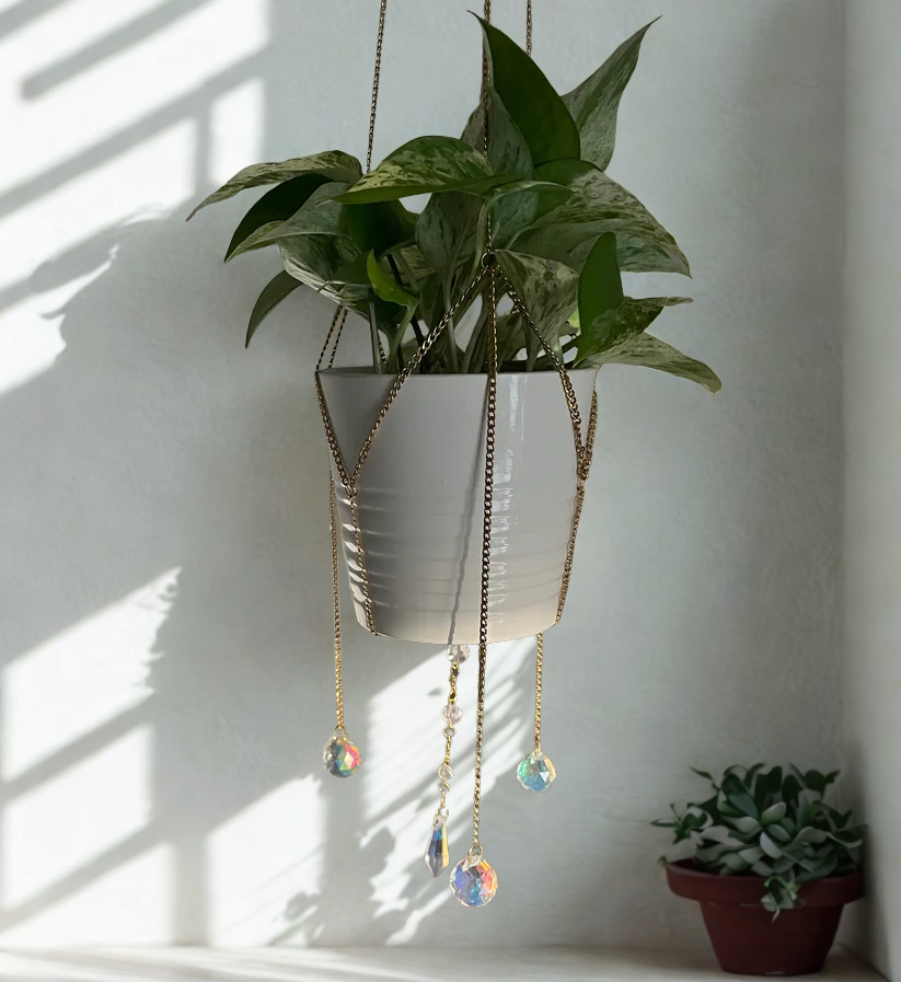 Hanging plant with decorative chains and crystal pendants against a white wall.