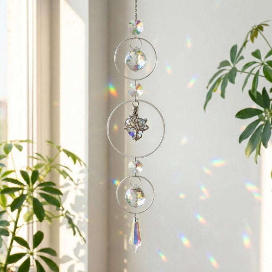 Crystal hanging ornament with rainbow effect in front of a window with plants.