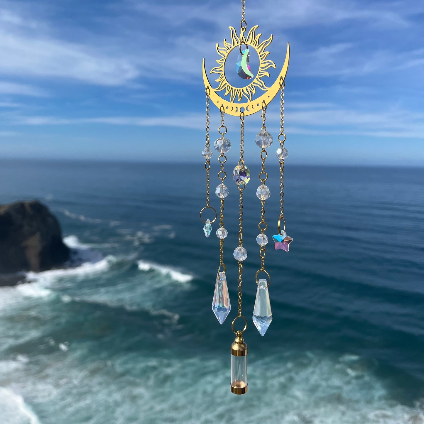 Decorative hanging ornament with celestial design against a blue sky and ocean background