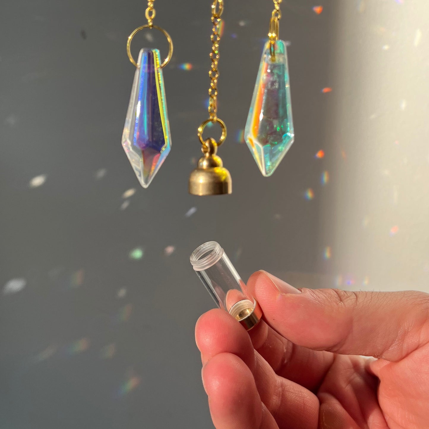 Hand holding a crystal pendant with more pendants on a reflective surface