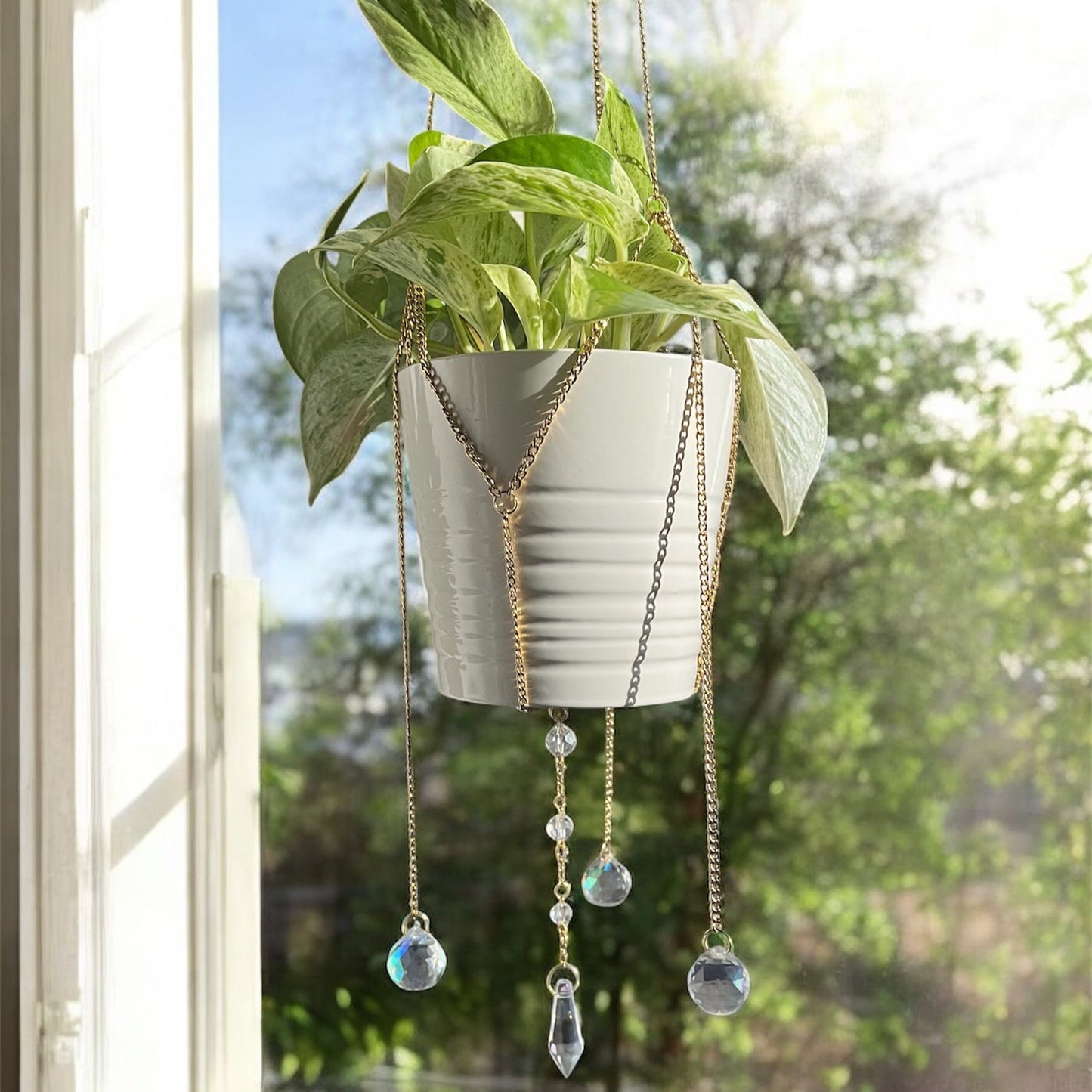 Hanging planter with decorative chains and beads in front of a window with a view of trees.
