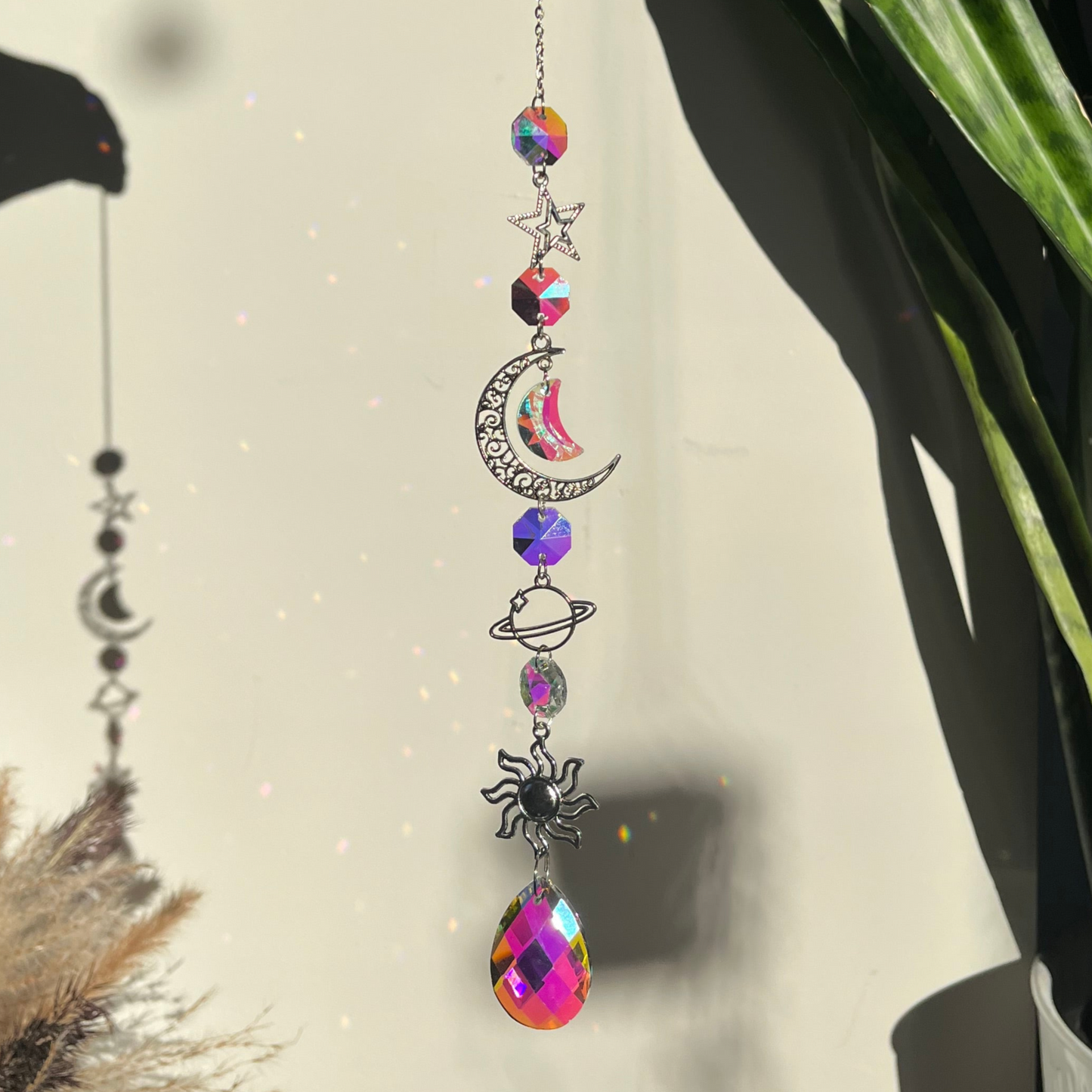 Decorative hanging charm with colorful crystals and celestial designs against a neutral background.