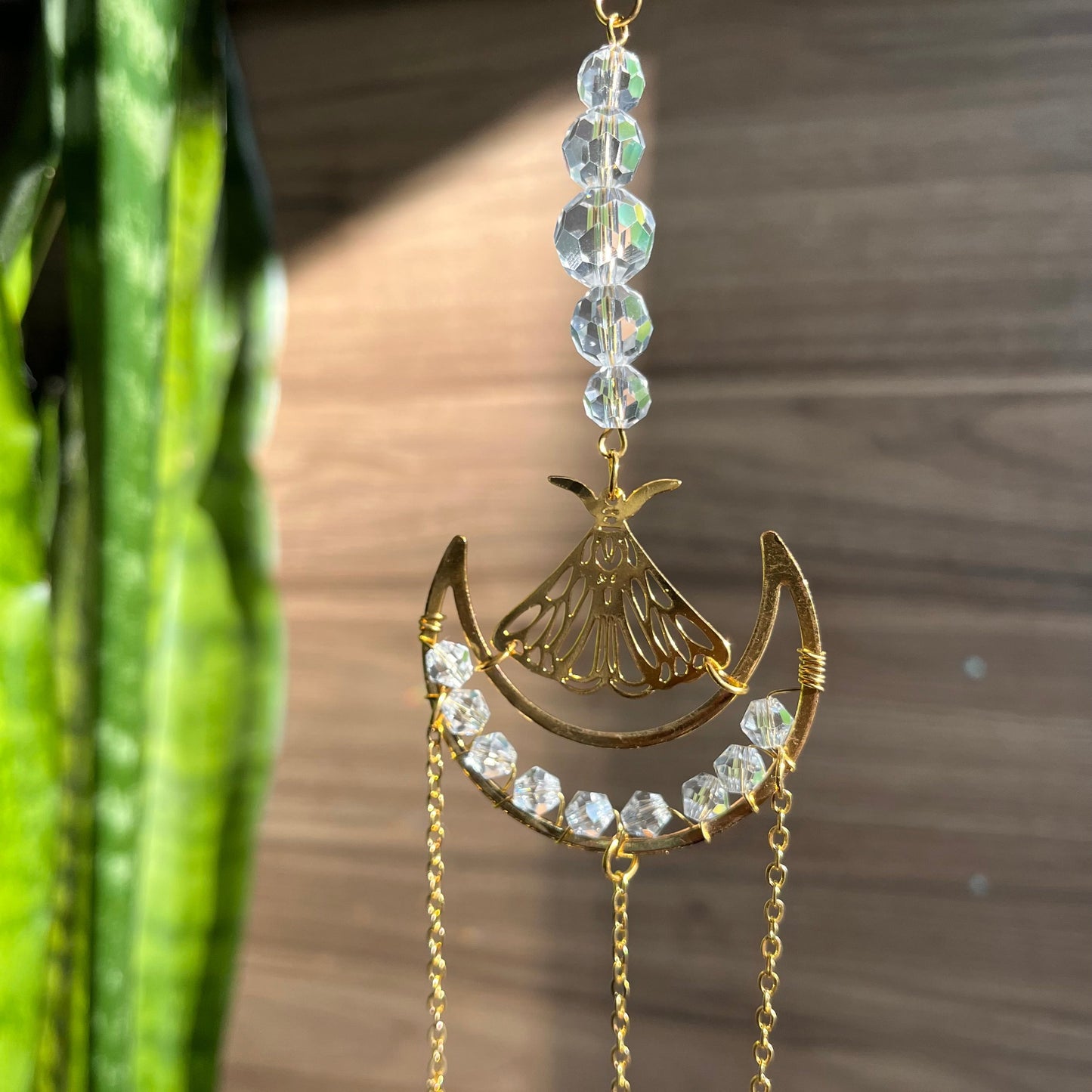 Decorative hanging ornament with crystals and gold elements against a wooden background
