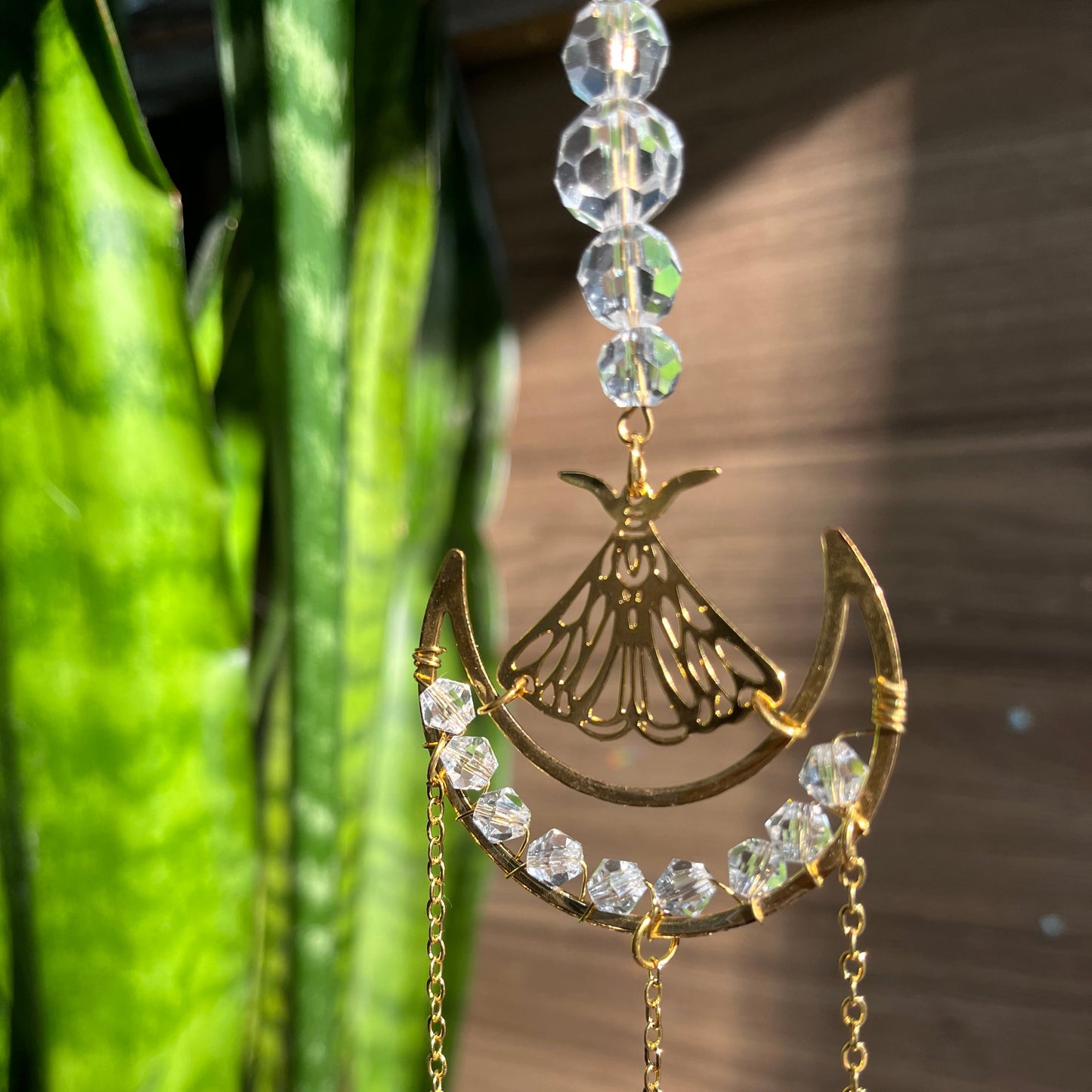 Decorative gold and crystal suncatcher against a blurred green plant background