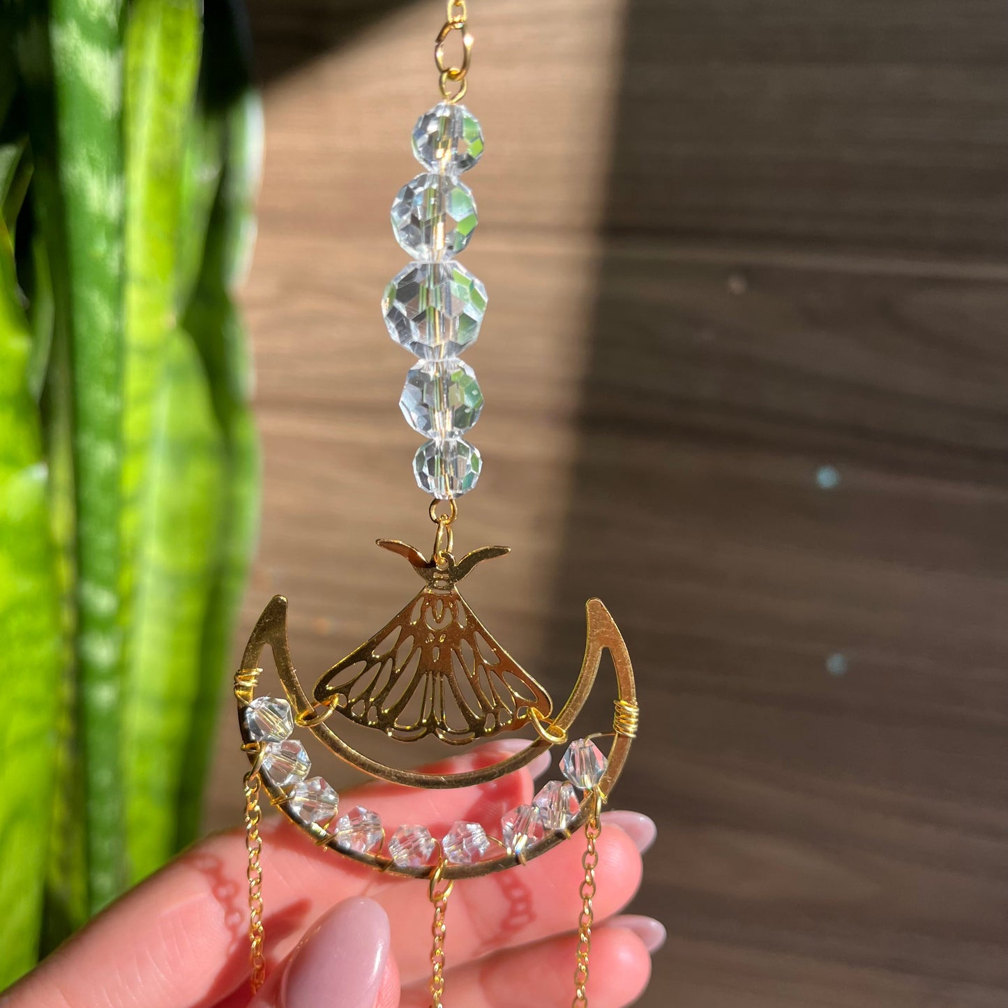 Decorative car charm with beads and gold accents held by a hand against a blurred background