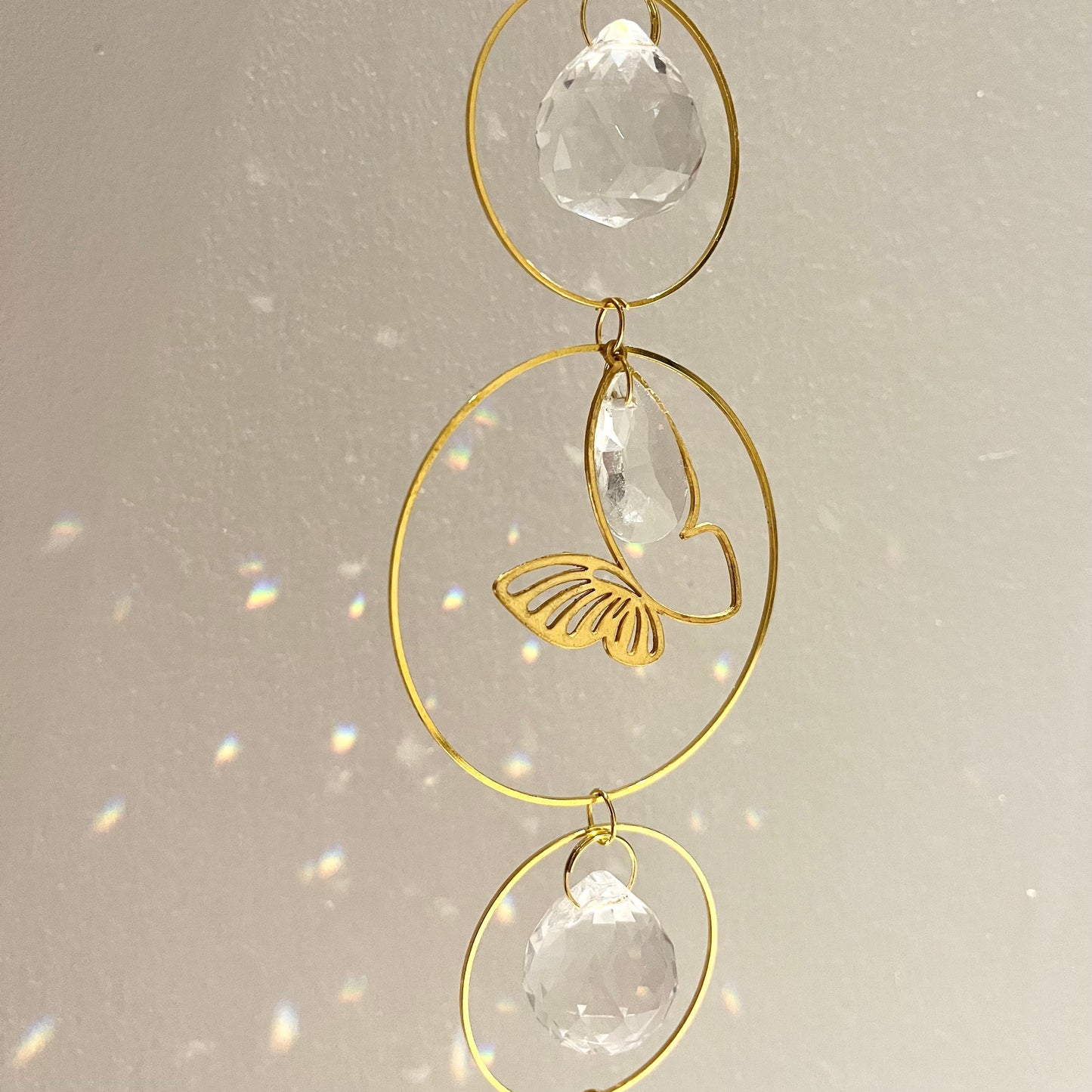 Decorative hanging ornament with gold loops and clear crystals on a light background