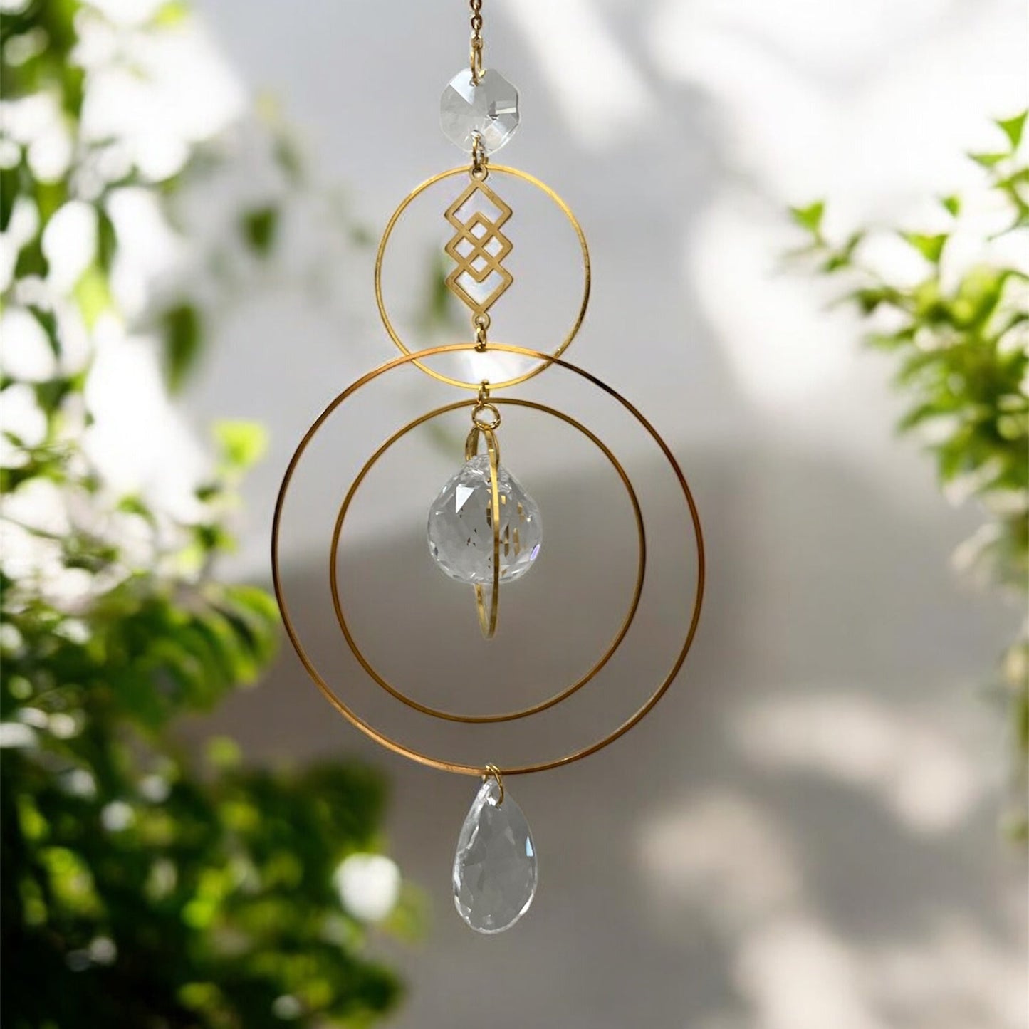 Decorative hanging ornament with gold loops and crystal-like elements against a blurred natural background