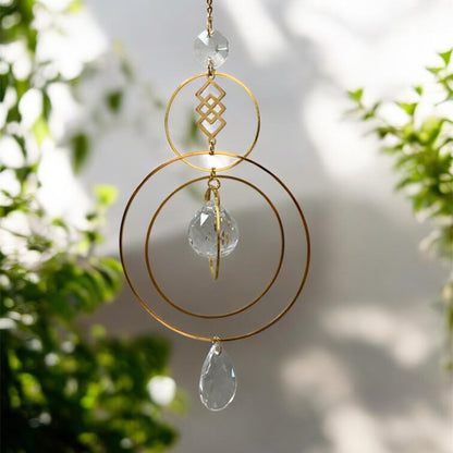 Decorative hanging ornament with gold loops and crystal-like elements against a blurred natural background