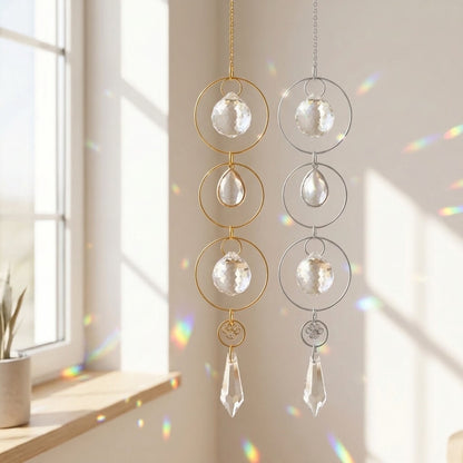 Two hanging crystal suncatchers with circular gold and silver frames are shown in a sunlit room near a window, with rainbow light reflections on the wall.