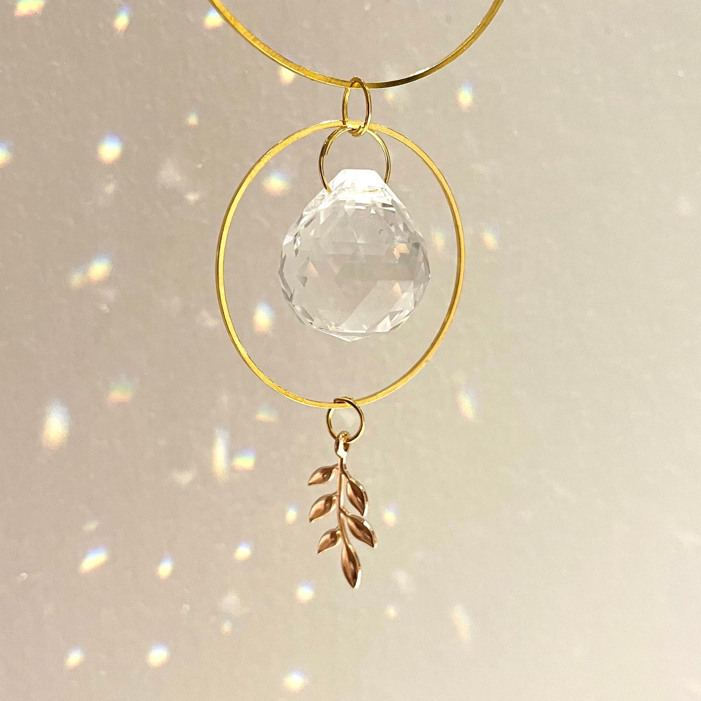 Decorative hanging ornament with gold loops, clear crystal ball, and leaf charm on a light background.