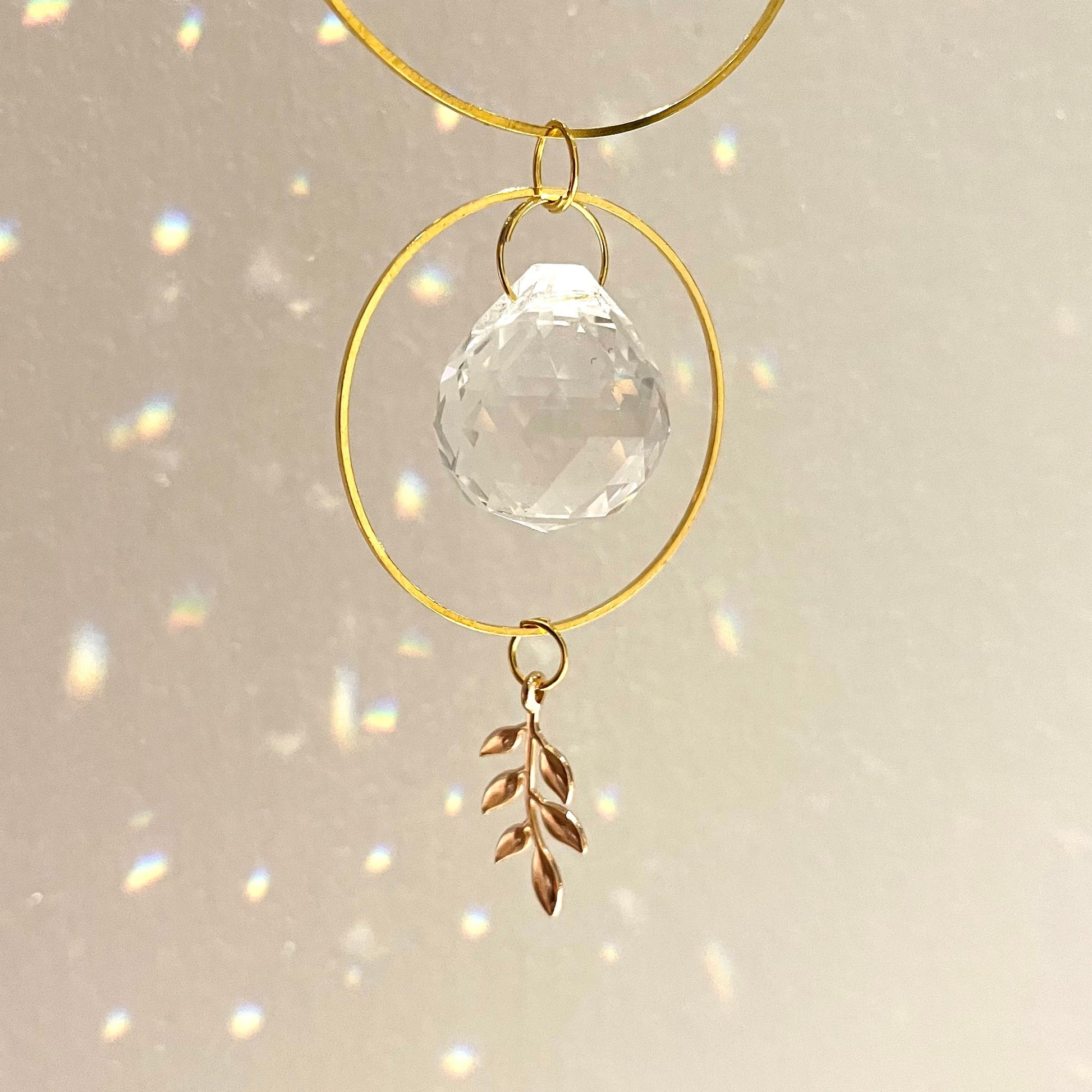 Decorative hanging ornament with gold loops, clear crystal ball, and leaf charm on a light background.