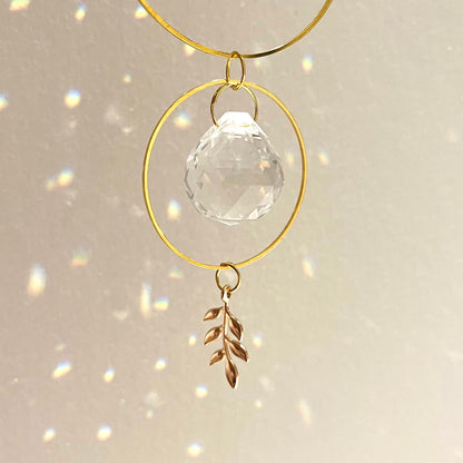 Decorative hanging ornament with gold loops, clear crystal ball, and leaf charm on a light background.