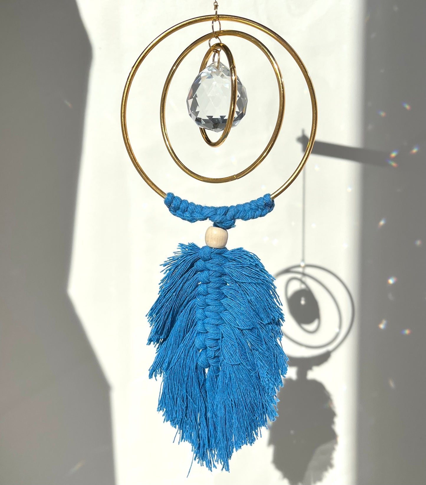 Decorative hanging ornament with blue tassels and a crystal on a plain background