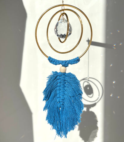 Decorative hanging ornament with blue tassels and a crystal on a plain background