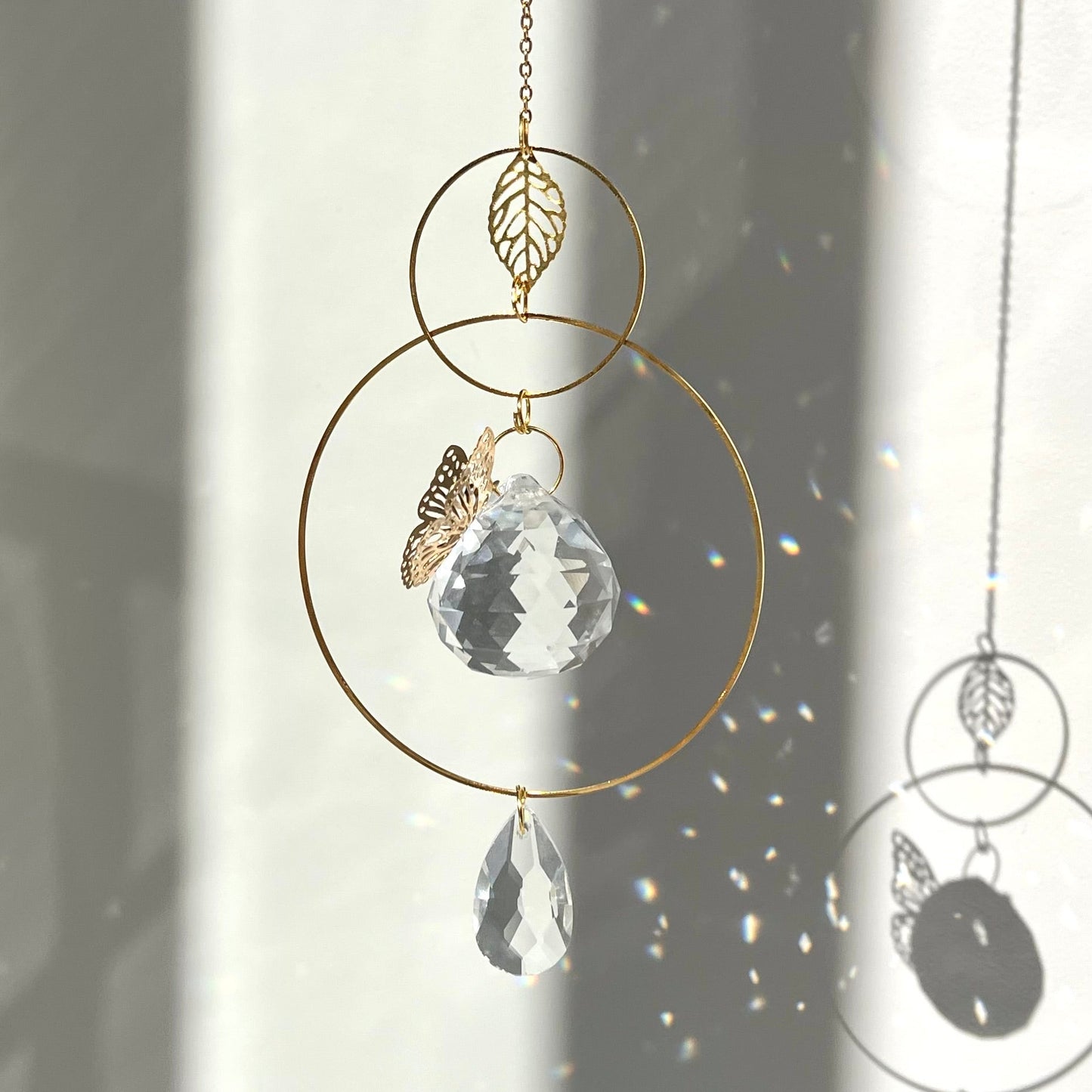 Decorative hanging crystal with gold chain and leaf charm against a light background