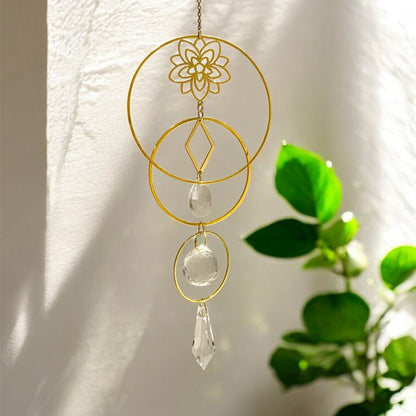 Decorative gold and crystal hanging ornament against a white wall with green leaves.