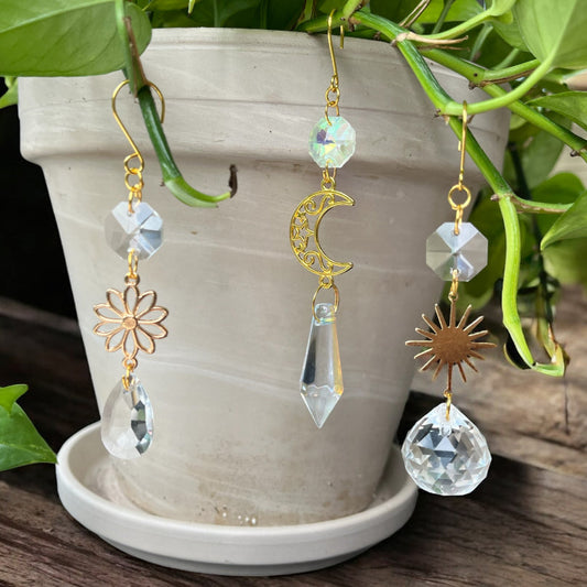 Gold earrings with crystal elements in front of a potted plant