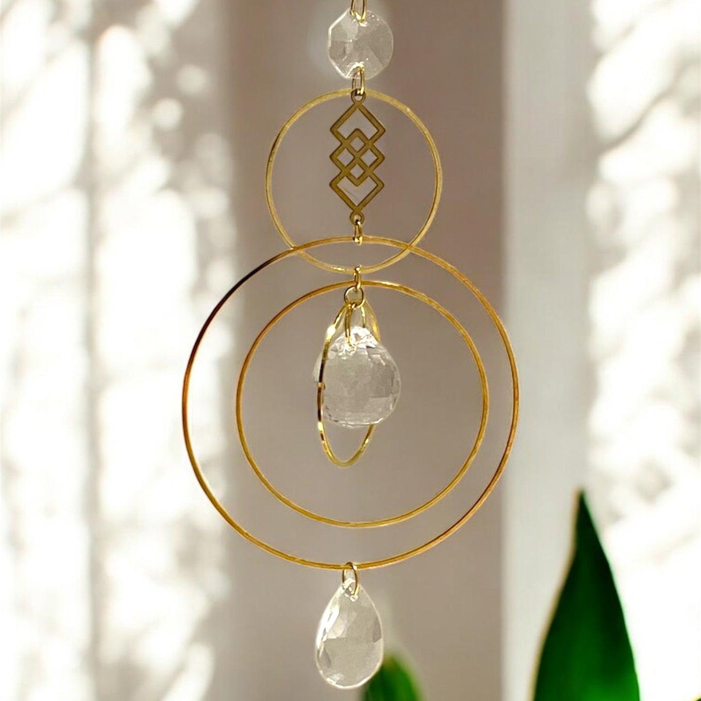 Decorative hanging crystal with gold loops and clear stones against a neutral background