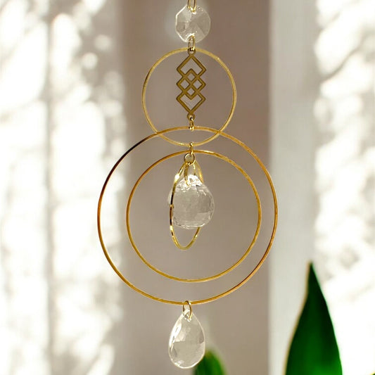 Decorative hanging crystal with gold loops and clear stones against a neutral background