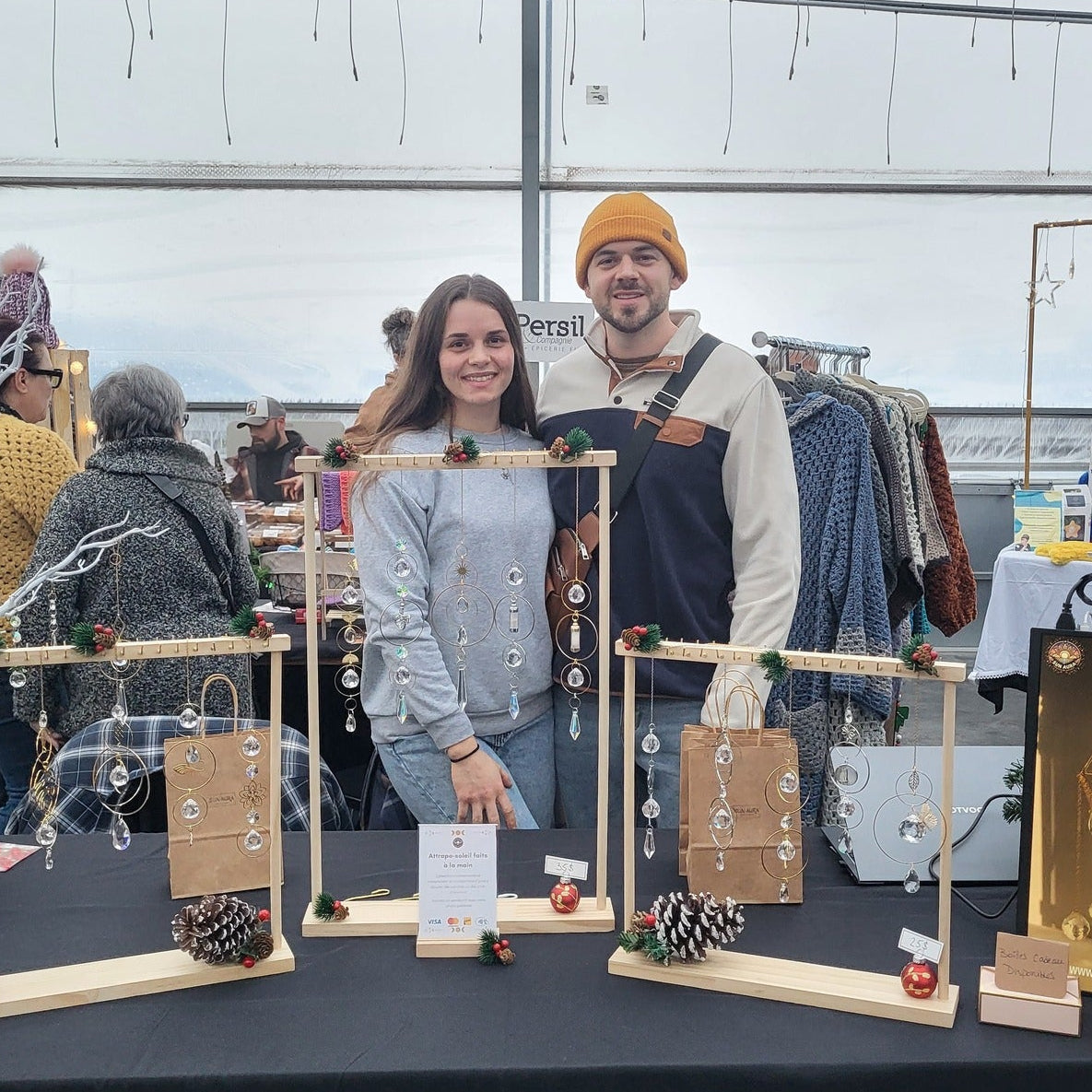 Two people standing behind a display of jewelry in a greenhouse setting.
