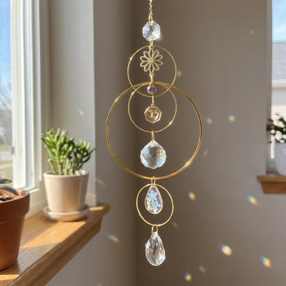 Decorative hanging crystal ornament with gold loops and clear crystals in a room with a window and plants.