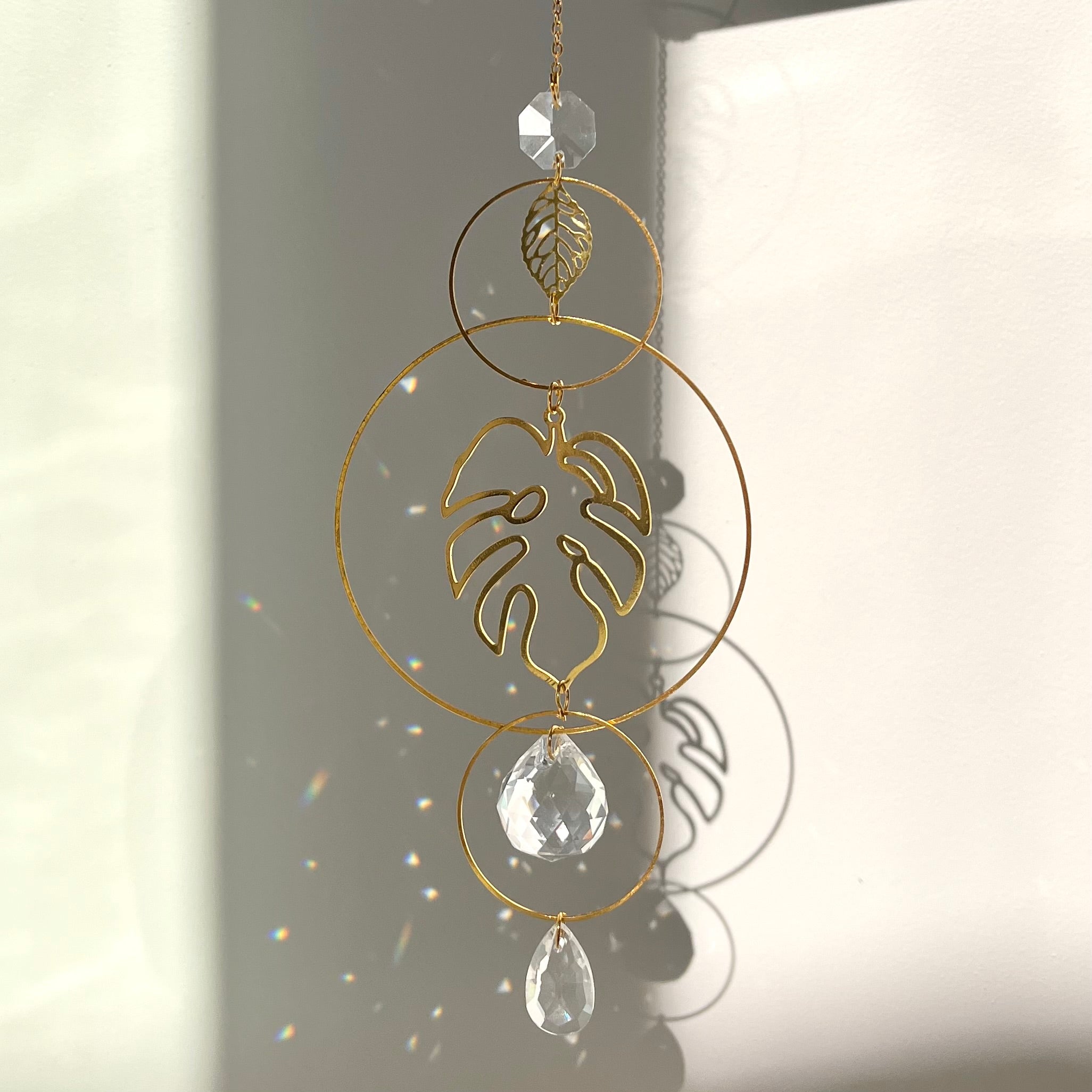 Decorative hanging ornament with gold loops and crystal elements on a neutral background