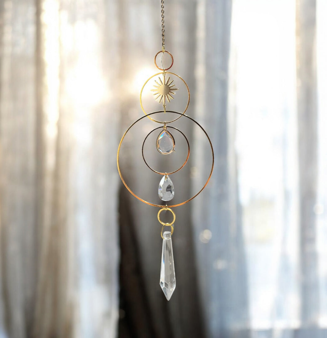 Decorative hanging crystal with gold loops and clear crystals against a blurred curtain background