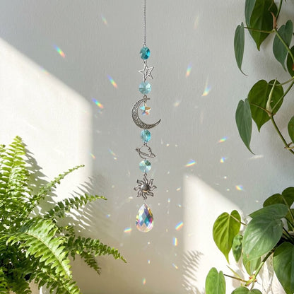 Decorative hanging crystal with celestial designs in front of a light gray wall with plants.