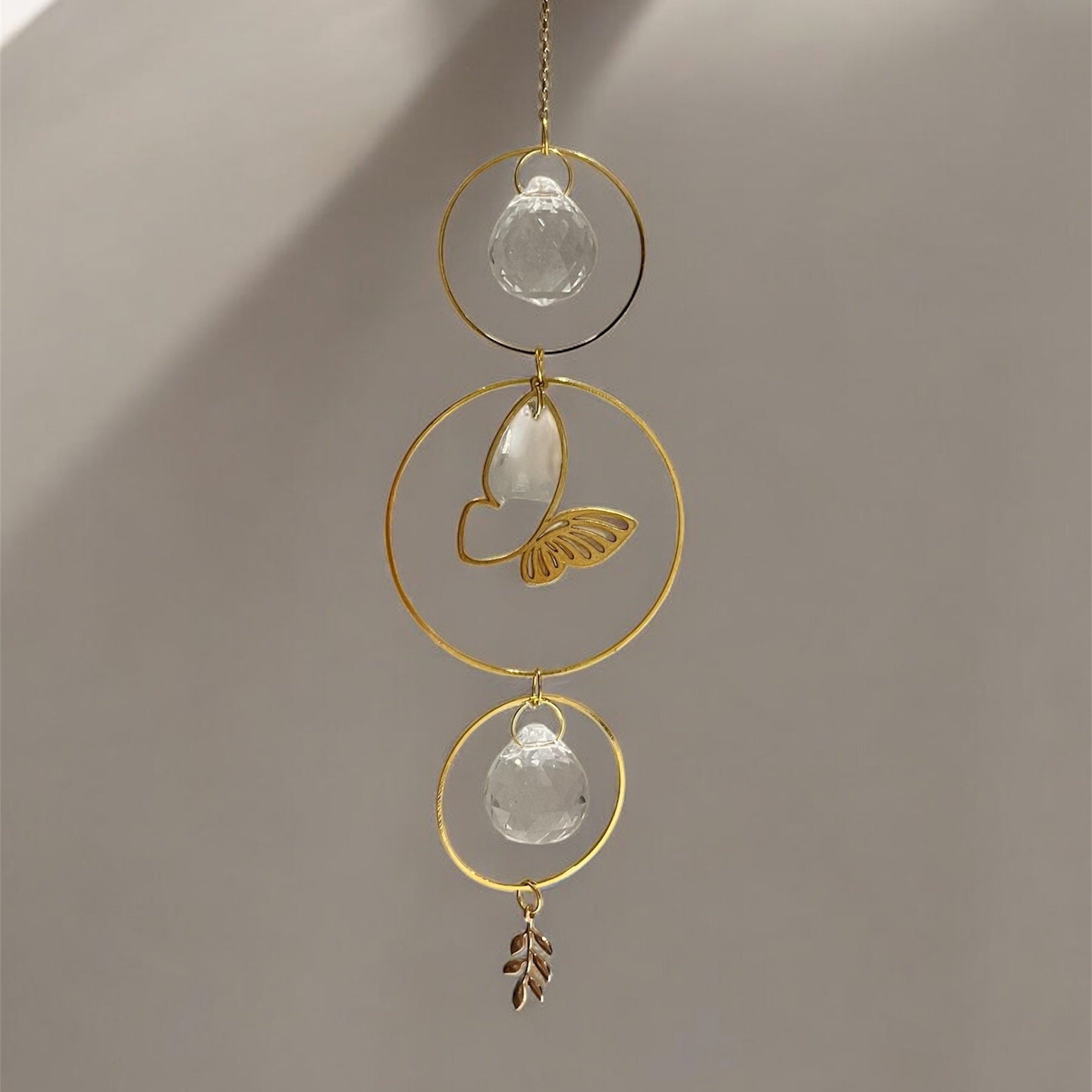 Decorative hanging ornament with gold loops and crystal-like elements on a neutral background