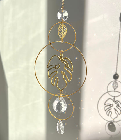 Decorative hanging ornament with gold loops, leaf design, and crystal-like elements on a light background.