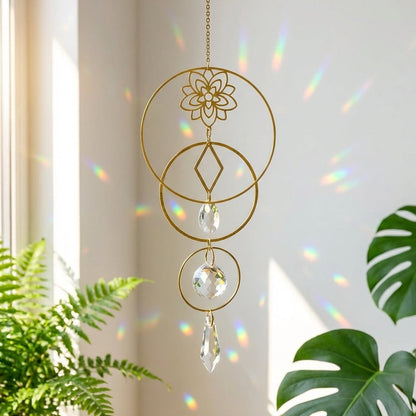 Decorative gold hanging ornament with crystal elements in front of a window with plants.