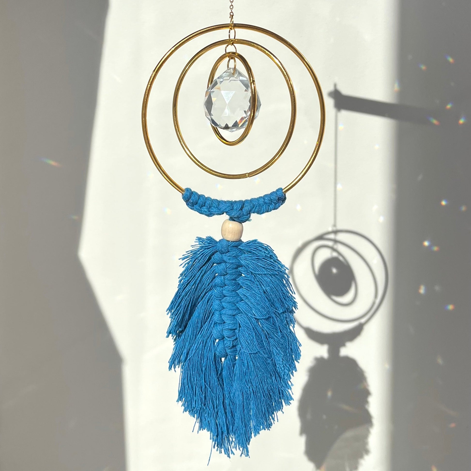 Decorative hanging ornament with blue tassels and a crystal on a white background
