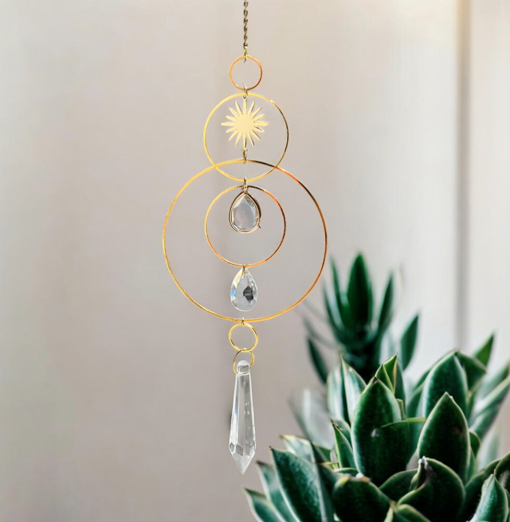 Decorative hanging crystal with gold loops and teardrop shapes in front of a plant.
