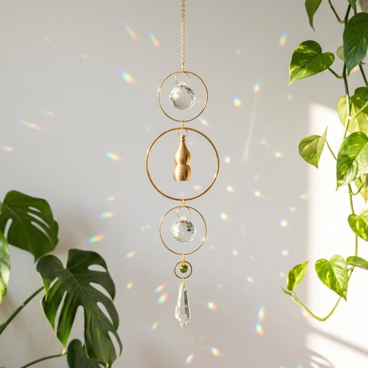 Decorative hanging crystal with gold accents on a light gray background with plants.
