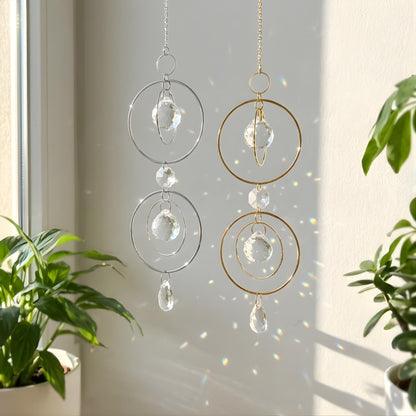 Crystal wind chimes hanging by a window with plants in the foreground