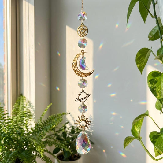 Decorative hanging crystal with celestial designs in front of a window with plants.