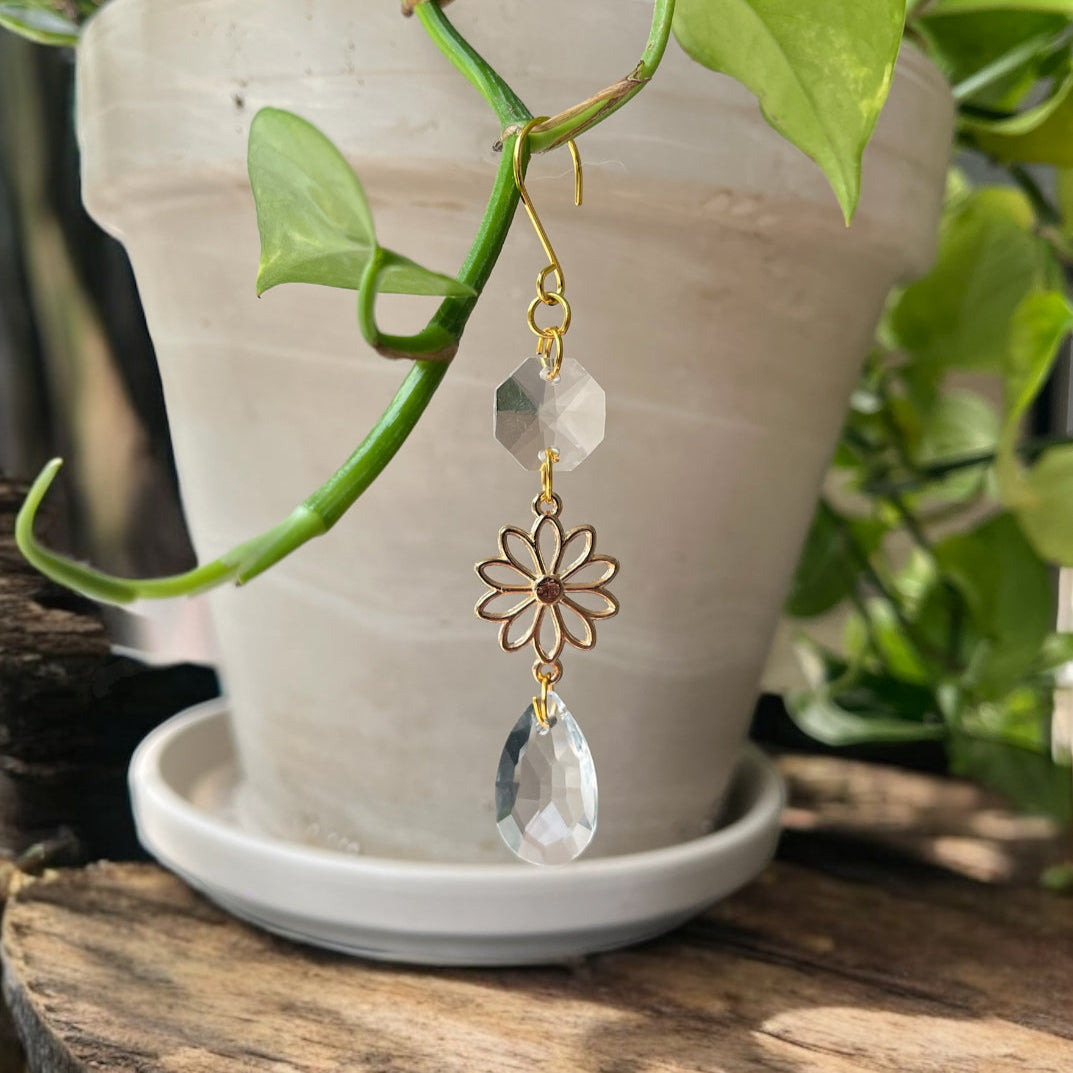 Gold and crystal earring hanging from a green plant with a pot in the background