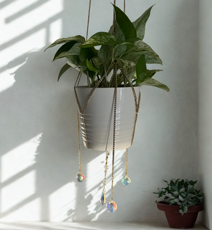 Hanging plant with decorative chains and crystal pendants against a white wall.