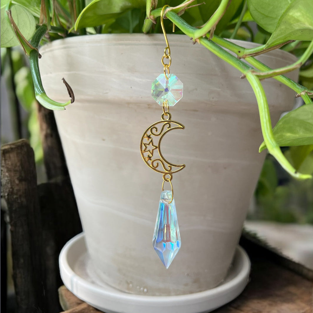 Decorative crystal moon and star hanging ornament in front of a potted plant.