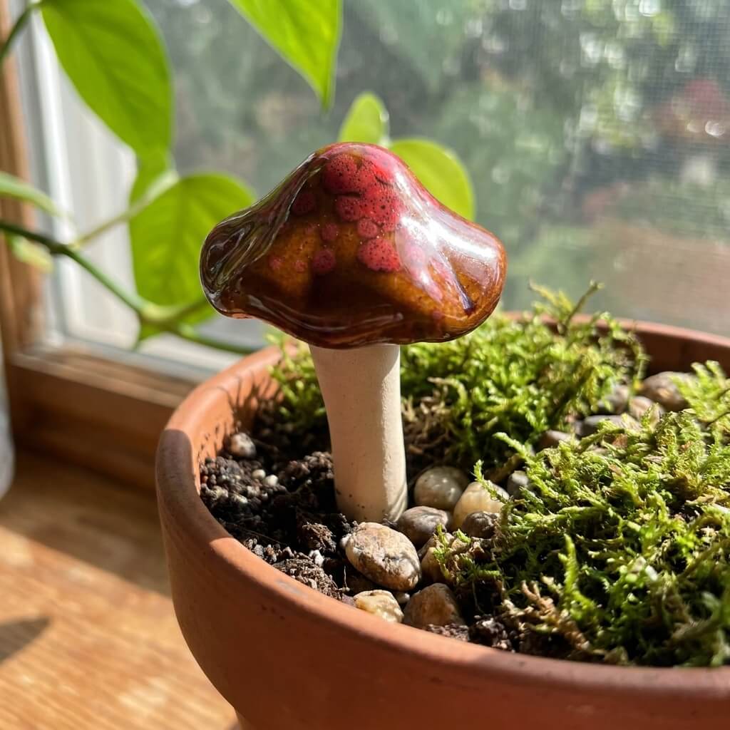 Mushroom-shaped decorative item in a pot with moss and stones on a windowsill.