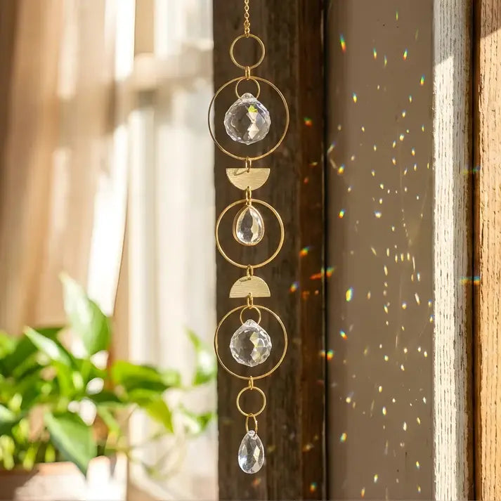 Decorative hanging crystal ornament with gold frame against a window background