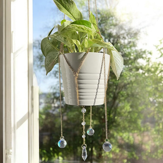Hanging planter with decorative chains and beads in front of a window with a view of trees.