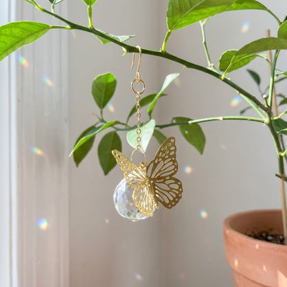 Gold butterfly earring with a clear crystal on a green plant background