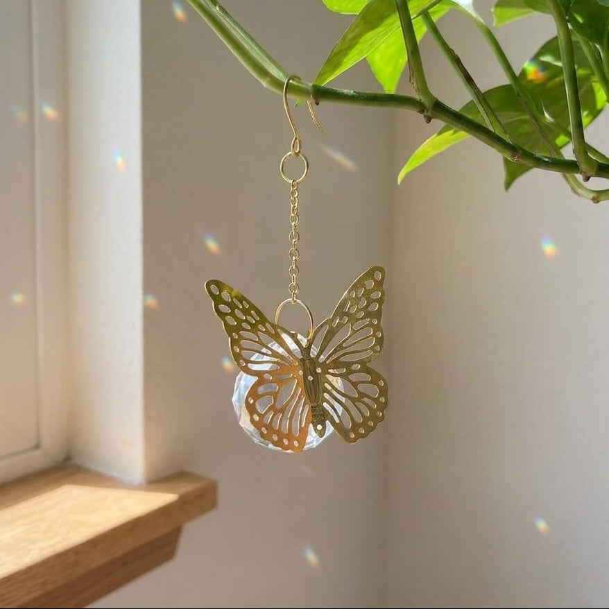 Gold butterfly-shaped decorative item hanging from a plant near a window