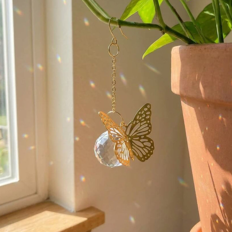 Gold butterfly ornament hanging from a plant near a window