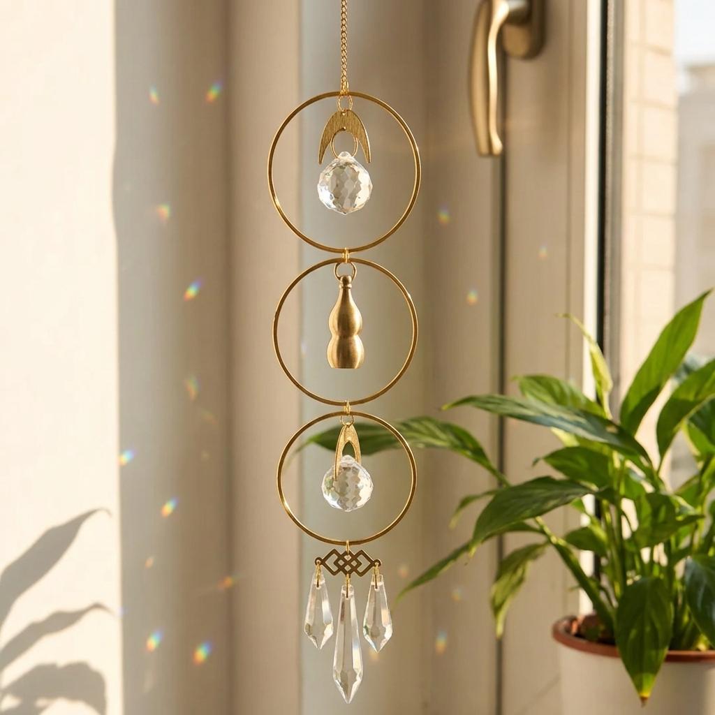 Decorative hanging crystal with gold accents in front of a window with a plant.