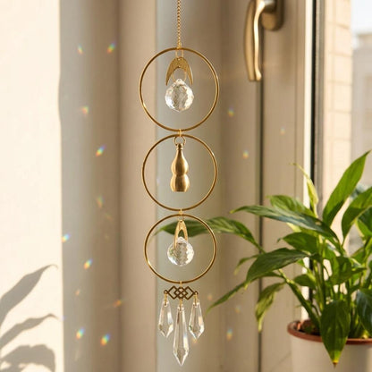 Decorative hanging crystal with gold accents in front of a window with a plant.