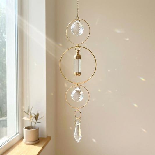 Decorative hanging crystal chime with gold frame against a neutral wall.